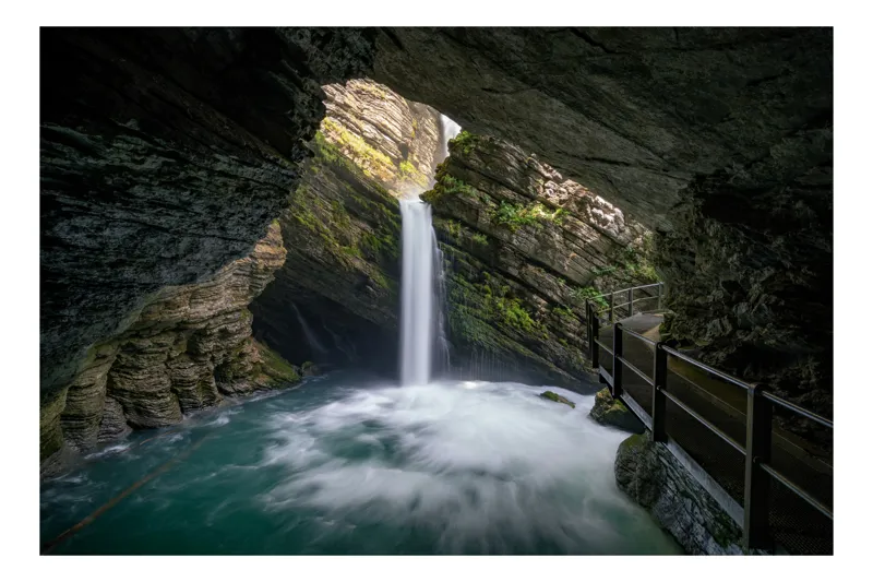 Tablou Canvas, "Cascada ascunsă în peșteră misterioasă", Cascadă, Peșteră, Apă, Stânci, Lumină, Vegetație, Podet, Mister, Frumusețe, Natură, 100 x 70 cm