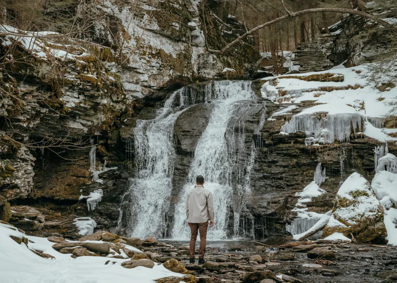 Tablou Canvas, "Om admira cascada înzăpezită iarna", Cascadă, Zăpadă, Gheață, Pădure, Roci, Figură Umană, Iarnă, Natură, Tranquilitate, Aventură, 70 x 50 cm – poza 2