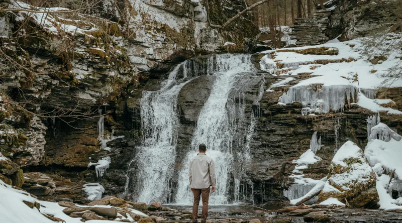 Tablou Canvas, "Om admira cascada înzăpezită iarna", Cascadă, Zăpadă, Gheață, Pădure, Roci, Figură Umană, Iarnă, Natură, Tranquilitate, Aventură, 90 x 50 cm – poza 2