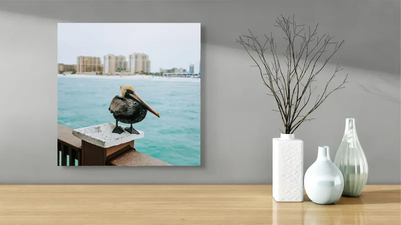 Tablou Canvas, "Pelican așezat pe balustradă la ocean", Pelican, Mare, Balustradă, Clădiri, Cer, Nori, Plajă, Apă, Oraș, Vedere., 50 x 50 cm – poza 3